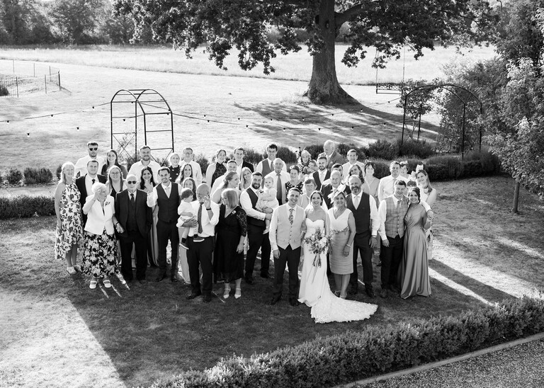 A black and white photo of guests on the lawn on a wedding day at Little Green Wedding Barn photographed by suffolk wedding photographer Hayley Denston Photography