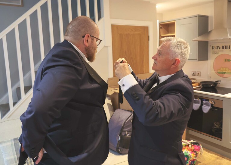 A grooms dad attempting to put on the grooms buttonhole  on a wedding day at Hungarian Hall Estate photographed by suffolk wedding photographer Hayley Denston Photography