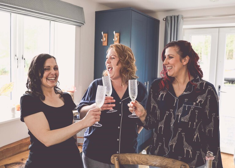 Bridesmaids laughing and having a glass of bubbly before they get dressed  on a wedding day at Hungarian Hall Estate photographed by suffolk wedding photographer Hayley Denston Photography