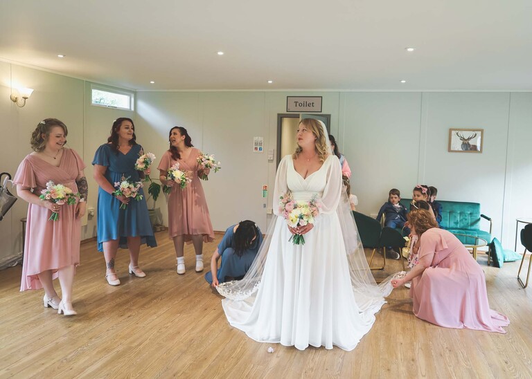 A bride having her dress arranged by bridesmaids before her ceremony  on a wedding day at Hungarian Hall Estate photographed by suffolk wedding photographer Hayley Denston Photography