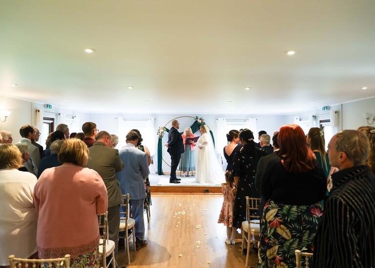 A bride and groom in front of a metal flower moon arch  on a wedding day at Hungarian Hall Estate photographed by suffolk wedding photographer Hayley Denston Photography