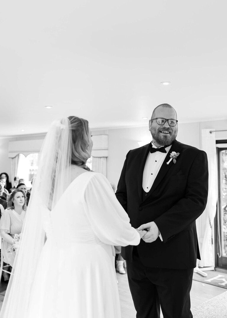 A black and white photo of a bride and groom exchanging vows  on a wedding day at Hungarian Hall Estate photographed by suffolk wedding photographer Hayley Denston Photography