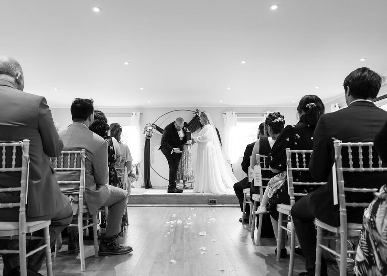 A black and white photo of a groom bowing to the guests during a wedding ceremony  on a wedding day at Hungarian Hall Estate photographed by suffolk wedding photographer Hayley Denston Photography
