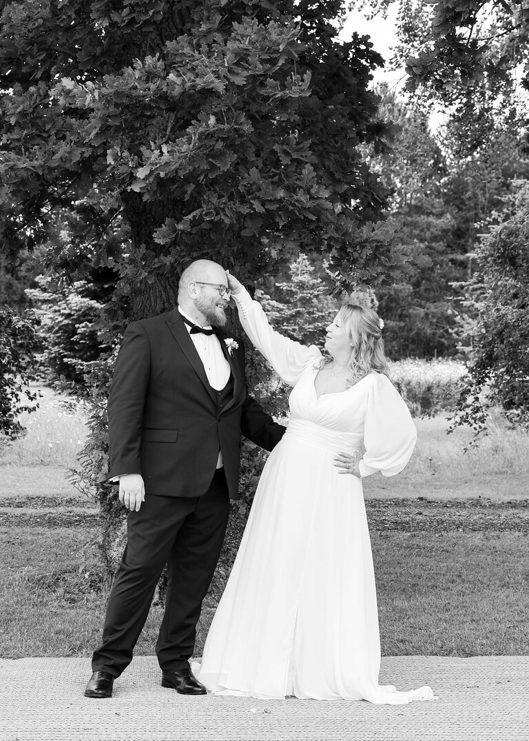 A black and white photo of a bride patting the groom on the head on a wedding day at Hungarian Hall Estate photographed by suffolk wedding photographer Hayley Denston Photography