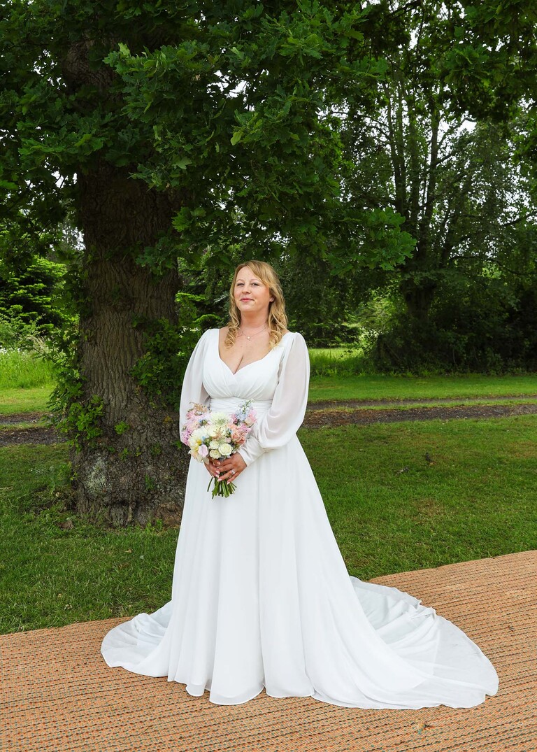 A bride stood under an old oak tree  on a wedding day at Hungarian Hall Estate photographed by suffolk wedding photographer Hayley Denston Photography