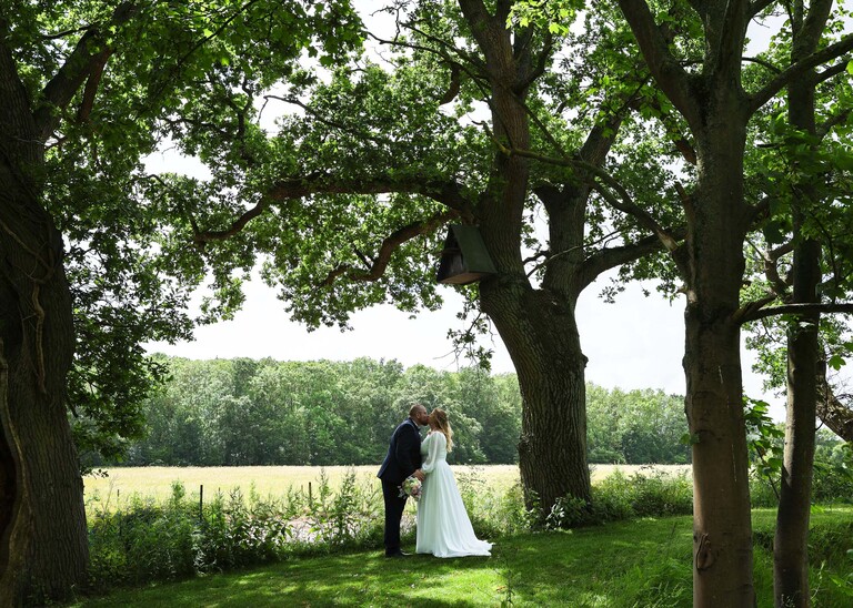 A bride and groom kissing under trees  on a wedding day at Hungarian Hall Estate photographed by suffolk wedding photographer Hayley Denston Photography
