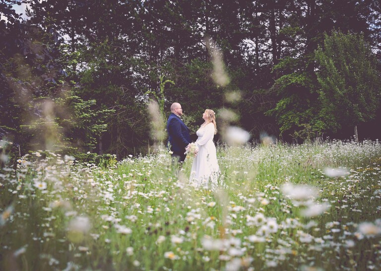 A bride and groom facing each other smiling in a wildflower meadow on a wedding day at Hungarian Hall Estate photographed by suffolk wedding photographer Hayley Denston Photography