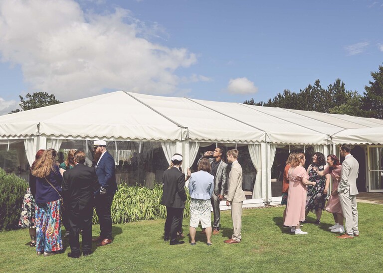 A wedding reception in gardens with a marquee in the background on a wedding day at Hungarian Hall Estate photographed by suffolk wedding photographer Hayley Denston Photography