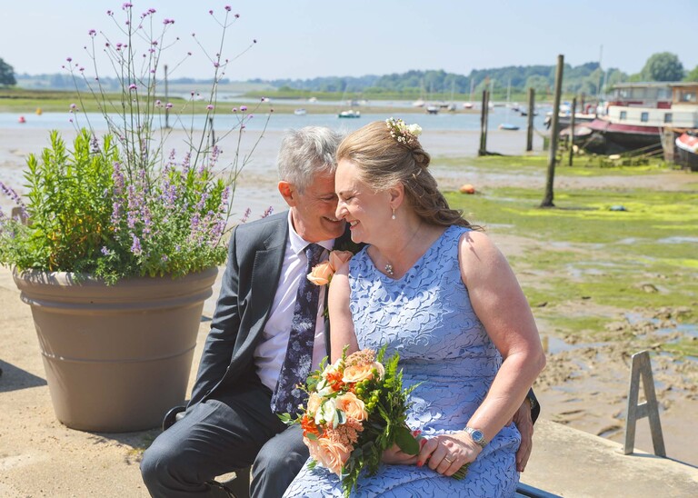 A bride and groom sat with their heads touching each other and woodbridge marina in the background on a wedding day in Woodbridge captured by Suffolk Wedding Photographer Hayley Denston Photography