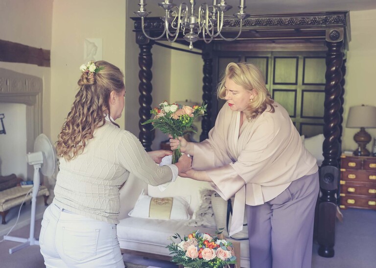 A bridesmaid passing the bride her flowers for drying in front of a four poster bed on a wedding day in Woodbridge captured by Suffolk Wedding Photographer Hayley Denston Photography