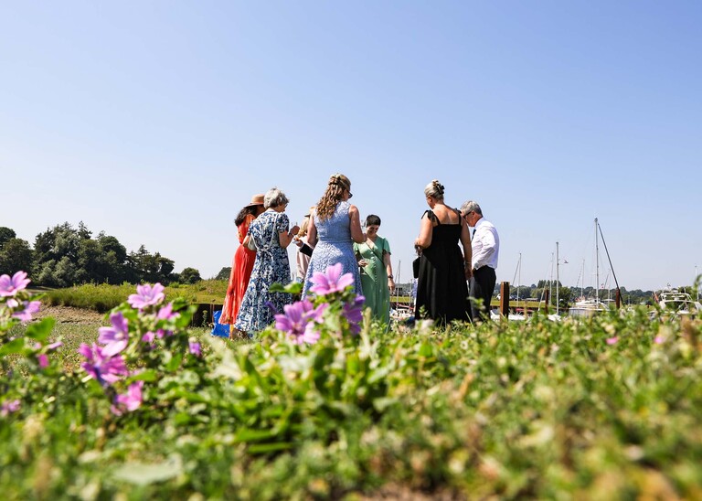 A bride and groom and their guests on the penisula at woodbridge marina on a wedding day in Woodbridge captured by Suffolk Wedding Photographer Hayley Denston Photography