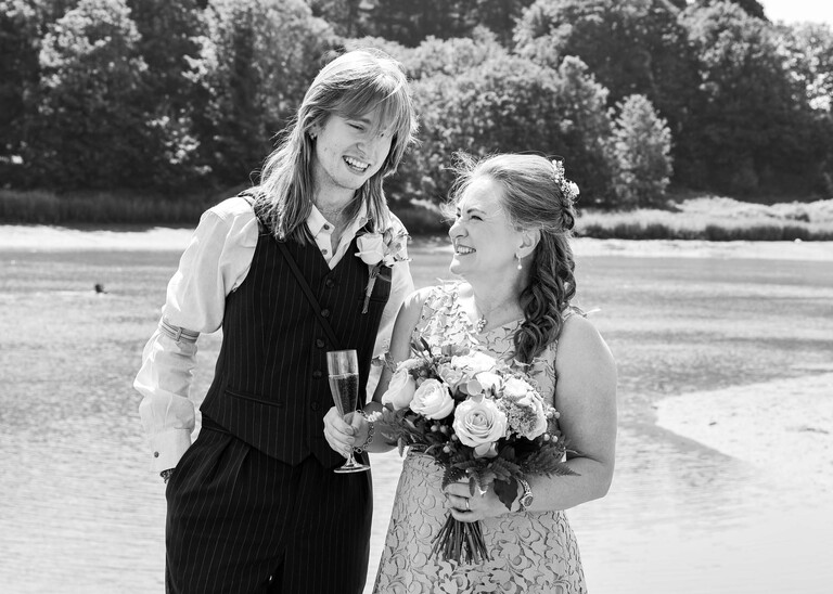 A black and white photo of a bride and her son laughing on the penisula at woodbridge marina on a wedding day in Woodbridge captured by Suffolk Wedding Photographer Hayley Denston Photography
