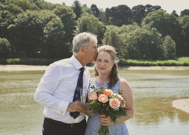 A groom kissing his bride on the head on the penisula at woodbridge marina on a wedding day in Woodbridge captured by Suffolk Wedding Photographer Hayley Denston Photography