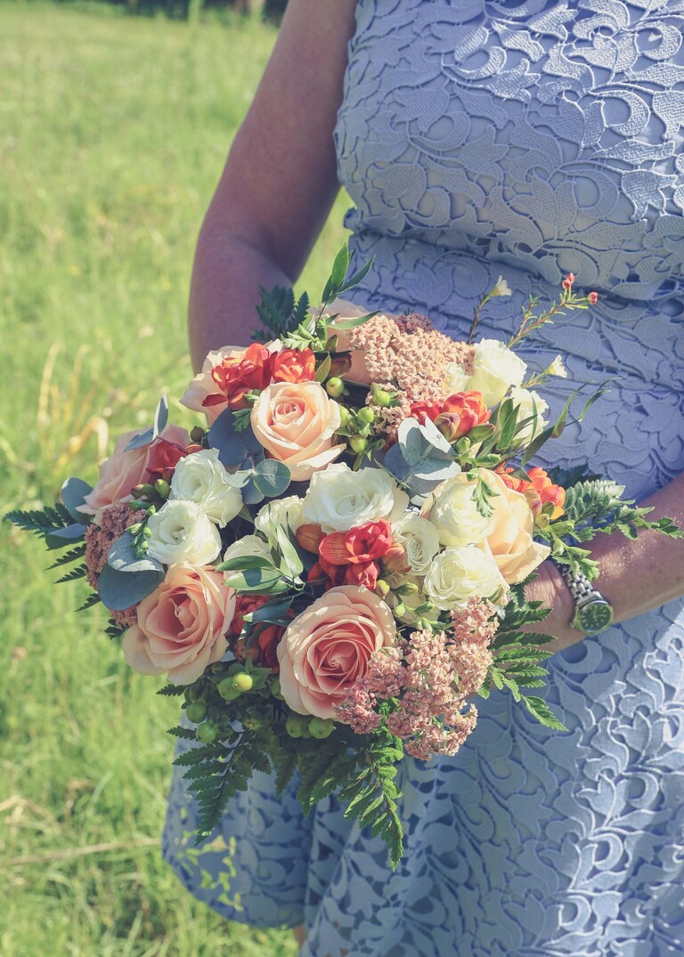 A bridal bouquet of orange and cream flowers on the penisula at woodbridge marina on a wedding day in Woodbridge captured by Suffolk Wedding Photographer Hayley Denston Photography 