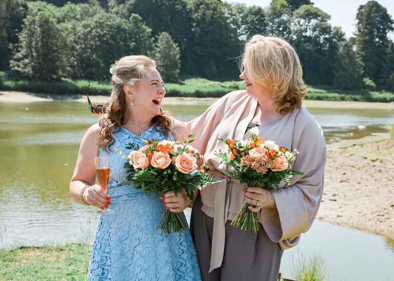 A bride and her bridesmaid looking at each other laughing on the penisula at woodbridge marina on a wedding day in Woodbridge captured by Suffolk Wedding Photographer Hayley Denston Photography