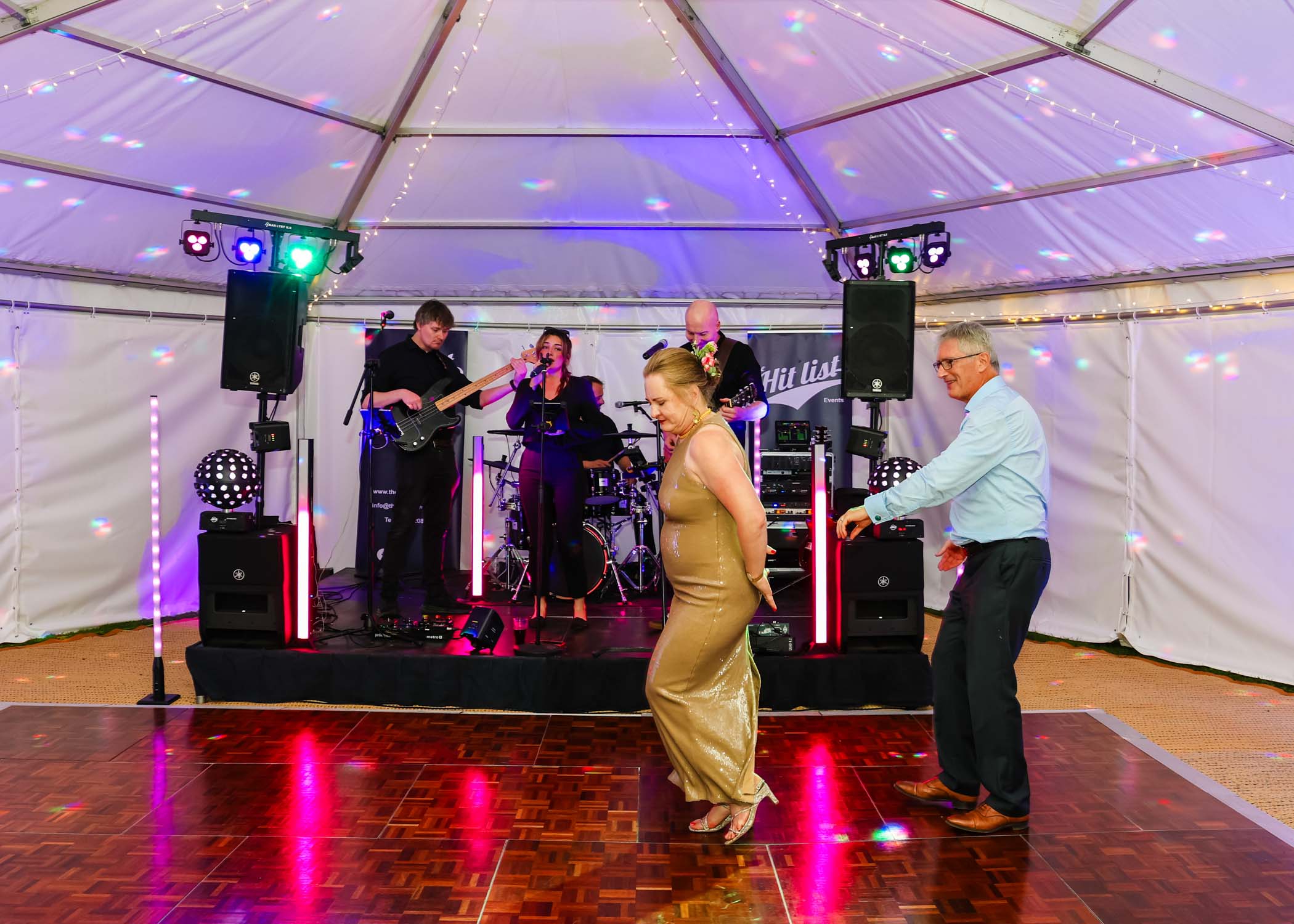 A bride and groom having their first dance with the band behind them in a lit marquee in gardens for an evening wedding reception at the Unruly Pig in Suffolk captured by Suffolk Wedding Photographer Hayley Denston Photography