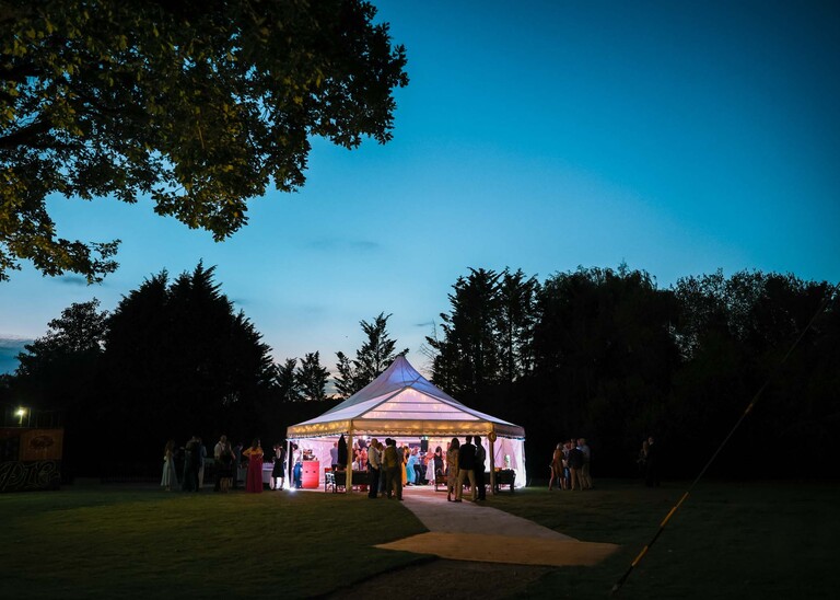 A lit marquee in gardens with everyone dancing for an evening wedding reception at the Unruly Pig in Suffolk captured by Suffolk Wedding Photographer Hayley Denston Photography